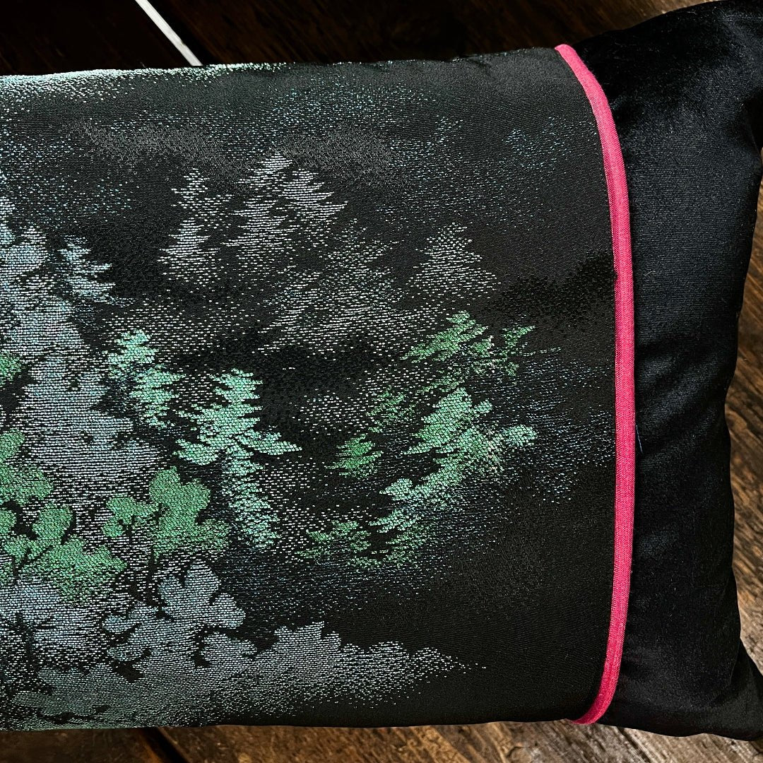Black silk has been embroidered with a scene of trees and mountains in pink and green metallic threads.